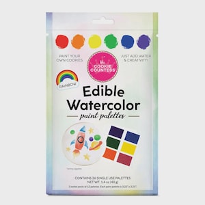 May include: A packet of edible watercolour paint palettes for cookies. The package features a rainbow, a rocket ship, and a planet design. The text on the package says "Paint Your Own Cookies" and "Just Add Water & Creativity!" Each palette is 8.26 cm x 8.26 cm.