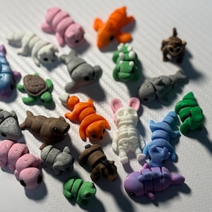 Pode incluir: Uma coleção de 19 pequenas figuras de animais pintadas à mão e coloridas. As figuras são feitas de um material liso e duro e têm cerca de 5 cm de altura. Os animais incluem uma tartaruga, um tubarão, um golfinho, uma raposa, um esqueleto, um macaco, um crocodilo e uma foca.