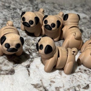 May include: A group of six small, beige pug figurines with black eyes and noses. The figurines are arranged in a circle on a light gray surface.