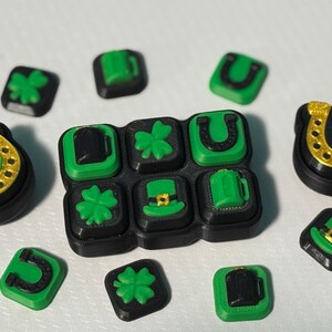 Può includere: Una collezione di oggetti decorativi a tema San Patrizio. Gli articoli includono disegni quadrati verdi e neri con trifogli, boccali di birra e cappelli da folletto. Ci sono anche disegni di ferri di cavallo e pentole d'oro.