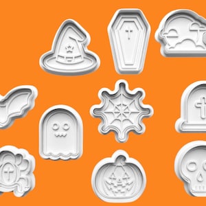 Może przedstawiać: Zbiór białych foremek do ciastek o tematyce Halloween na pomarańczowym tle. Foremki obejmują kształty takie jak kapelusz czarownicy, trumna, nagrobek, nietoperz, duch, pajęczyna, dynia, czaszka i ozdobny emblemat.