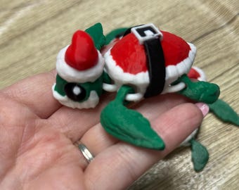 May include: A whimsical Christmas turtle figurine. The turtle's shell is red with a white trim, and a black belt. The head is green with a Santa hat. The turtle's flippers are green. A festive holiday decoration.