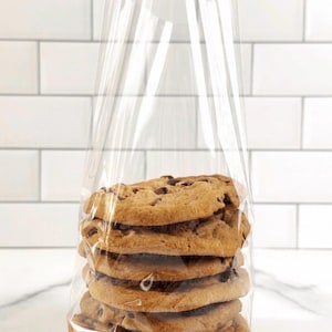 May include: A stack of six chocolate chip cookies in a clear cellophane bag. The cookies are golden brown with visible chocolate chips. The bag is transparent, allowing a clear view of the baked goods.