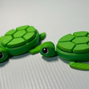 Puede incluir: Tres figuras de tortugas verdes con caparazones detallados y ojos expresivos. Las tortugas son de varios tamaños, la más grande mide aproximadamente 7.6 cm de largo. Las figuras están hechas de un material verde sólido.