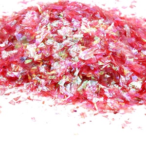 Puede incluir: Un montón de escamas rosas iridiscentes, posiblemente purpurina o material decorativo, sobre un fondo blanco. Las escamas tienen una cualidad brillante y reflectante, captando la luz y creando un efecto brillante. Ideal para manualidades y decoraciones.