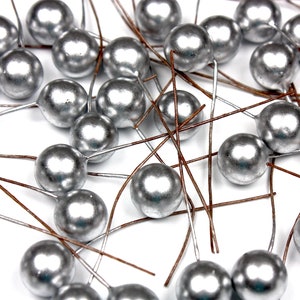 Op de afbeelding: Een verzameling zilverkleurige ronde ornamenten met draadstengels. De ornamenten zijn verspreid over een witte achtergrond.