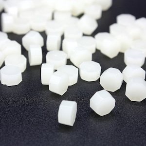 May include: A close-up of a pile of white wax sealing beads. The beads are hexagonal in shape and are scattered on a black surface.