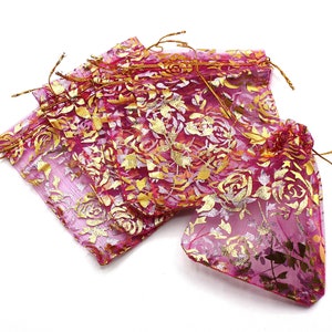 Puede incluir: Un conjunto de bolsas de regalo de organza rosa y dorada con cordones de cierre dorados. Las bolsas están hechas de tela transparente con un patrón floral y son perfectas para pequeños regalos o favores.