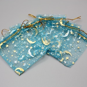 May include: A set of blue organza gift bags with gold stars and crescent moons printed on them. The bags have gold drawstring closures.