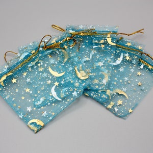 Puede incluir: Un conjunto de bolsas de regalo de tul azul con estrellas doradas y medias lunas impresas en ellas. Las bolsas tienen cierres de cordón dorado.