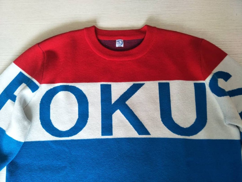 May include: A red, white, and blue striped sweater with the word "FOKUS" in blue letters on the white stripe.
