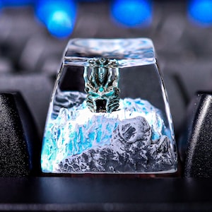 May include: A clear resin keycap with a detailed, blue and white, 3D printed design of a creature. The keycap is on a black keyboard.