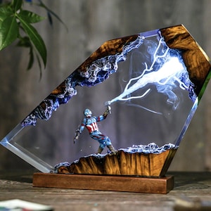 May include: A decorative resin sculpture featuring a Captain America figurine wielding a hammer, with a lightning bolt effect. The sculpture is encased in a clear, angled resin block with a wooden base and trim, creating a unique display piece.
