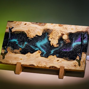 May include: A wooden serving tray with a black resin inlay featuring a swirling blue and purple design. The tray has two black metal handles and sits on a wooden stand.