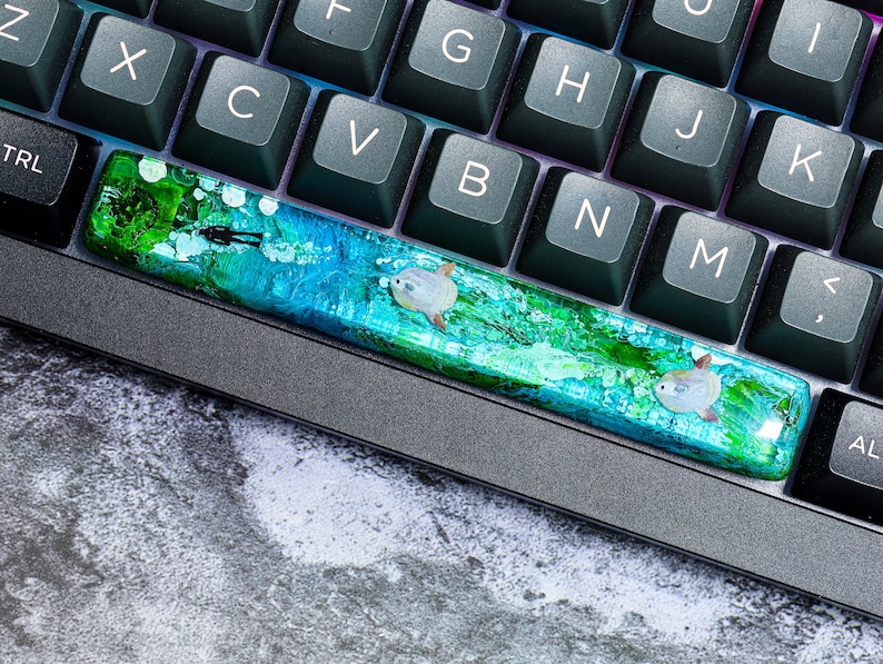 May include: A keyboard with a custom keycap featuring a blue and green abstract design with white fish. The keycap is made of resin and has a glossy finish.