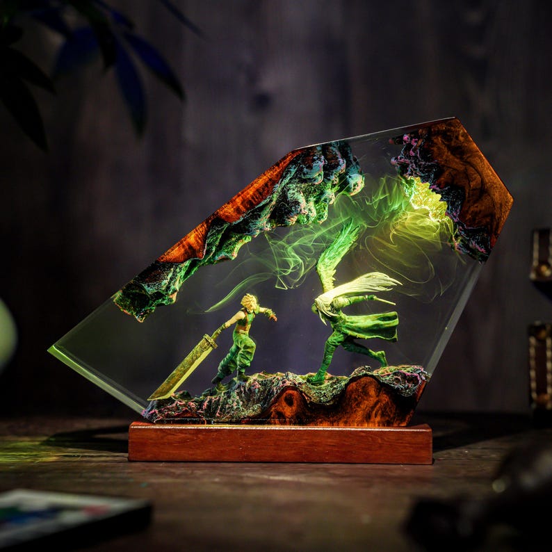 May include: A resin art piece featuring two figures in a battle scene, encased in clear resin. The figures are green and gold, set against a backdrop of green and orange rock formations. The base is made of wood.