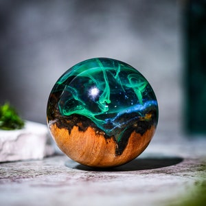 May include: A round, wooden orb with a dark brown wood base and a clear resin top filled with swirling green and blue resin.