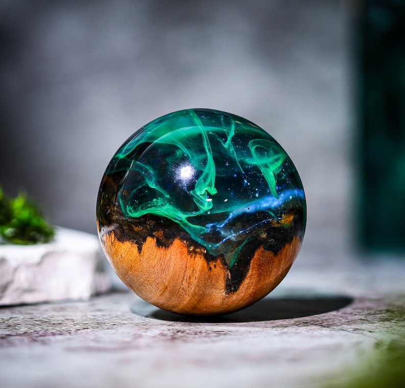 May include: A round, wooden orb with a dark brown wood base and a clear resin top filled with swirling green and blue resin.