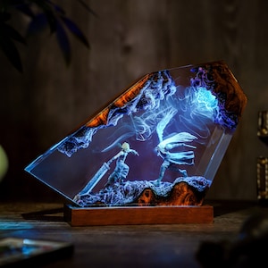 May include: A decorative resin sculpture featuring two figures in combat, set within a clear, angled block. The sculpture has a wooden base and is illuminated with blue and white light, with wood grain accents.