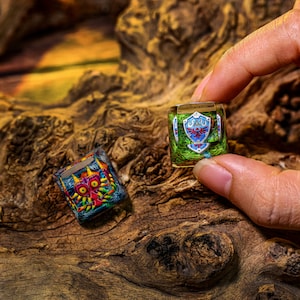 May include: Two resin keycaps featuring characters from the Legend of Zelda video game series. One keycap is green and blue with the Triforce symbol and the other is multi-colored with a red and yellow mask.