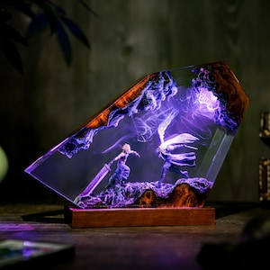 May include: A decorative resin lamp featuring a battle scene with two figures, illuminated by purple light. The lamp has a wooden base and a geometric shape with a wooden frame. The figures are set against a backdrop of swirling purple smoke.