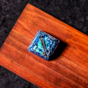 May include: A blue and green resin keycap with a silver anchor design. The keycap is square shaped and has a glossy finish.