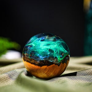 May include: A round, wooden orb with a clear resin top filled with swirling green and blue resin. The resin looks like a galaxy or nebula.
