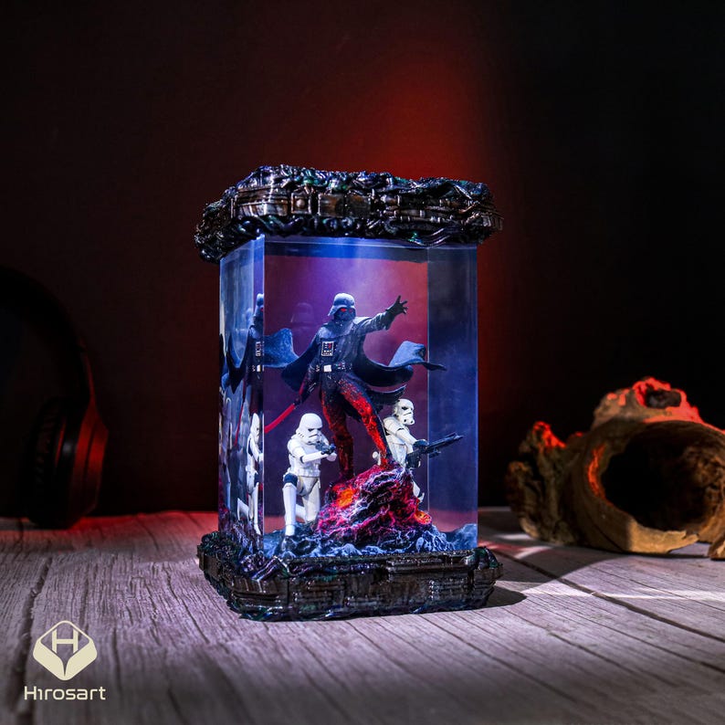 K&ouml;nnte beinhalten: Eine gl&auml;serne Vitrine mit einer schwarzen und roten Darth Vader Figur und zwei wei&szlig;en Stormtrooper Figuren. Die Vitrine ist von innen mit blauem Licht beleuchtet und hat einen schwarzen Sockel.