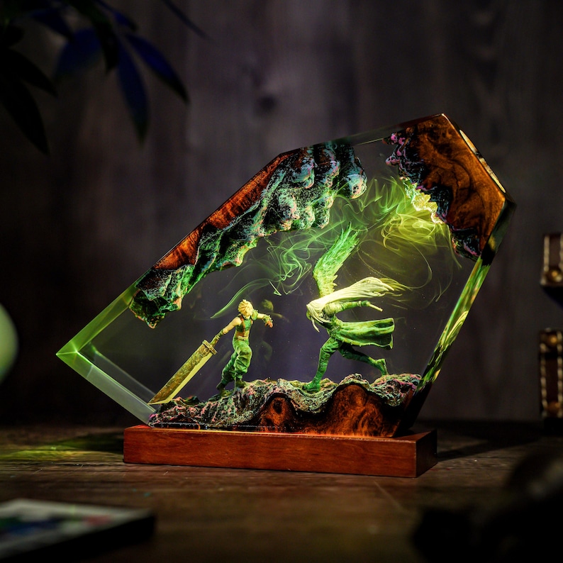 May include: A unique resin art piece featuring a battle scene with two figures, one with a sword. The artwork is encased in a clear, angled block with a wooden base. The scene is illuminated with green and yellow light.
