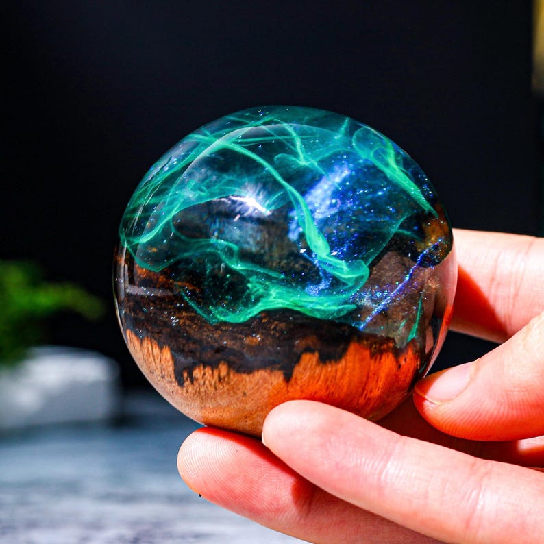 May include: A dark wood sphere with a clear resin top filled with swirling green and blue glitter.