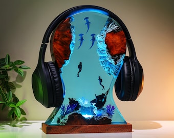 May include: A blue resin headphone stand with a design of a coral reef and hammerhead sharks. The stand has a pair of black headphones attached to it.