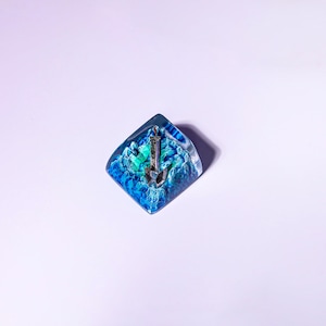 May include: A blue and green resin keycap with a silver anchor design.