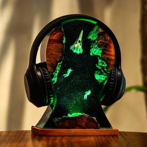 May include: A black headphone stand with a green resin base featuring a spaceship and astronauts. The stand is illuminated with green LED lights.