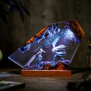 May include: A resin art piece featuring two figures in combat, set against a backdrop of swirling blue and white light. The artwork is encased in a clear, angled resin block with a wooden base, showcasing a detailed fantasy scene.