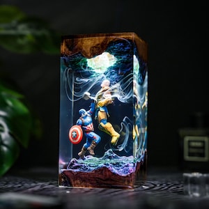 May include: A rectangular resin lamp featuring a miniature scene of Captain America holding a shield and fighting Thanos, who holds a hammer. The clear resin block has swirling white smoke effects, a glowing light source, and a textured base.