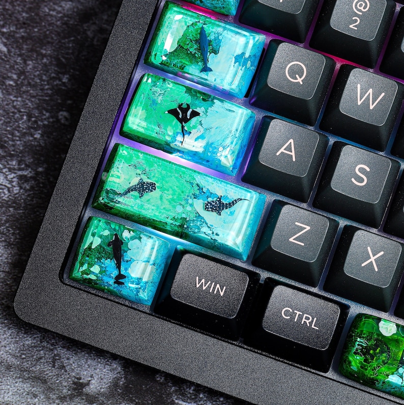 May include: A black keyboard with custom keycaps featuring a blue and green ocean-themed design. The keycaps have images of manta rays, sharks, and other sea creatures. The keyboard has keys labeled 'WIN', 'CTRL', 'Z', 'X', 'S', 'A', 'Q', 'W', and '2'.
