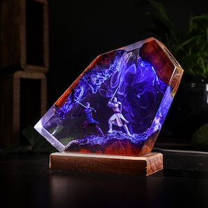 May include: A resin sculpture featuring two figures with lightsabers in a battle scene. The sculpture is encased in clear resin with a blue and purple nebula effect, set on a wooden base. The edges are framed with wood.
