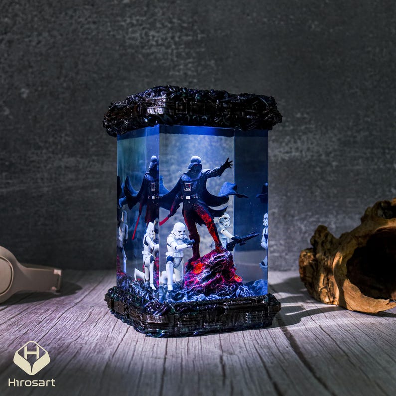 K&ouml;nnte beinhalten: Eine dunkelblaue Harzlampe mit einem klaren W&uuml;rfel, der eine Miniatur-Szene mit Darth Vader und Stormtroopers enth&auml;lt. Die Szene wird von unten beleuchtet, wodurch ein leuchtender Effekt entsteht.