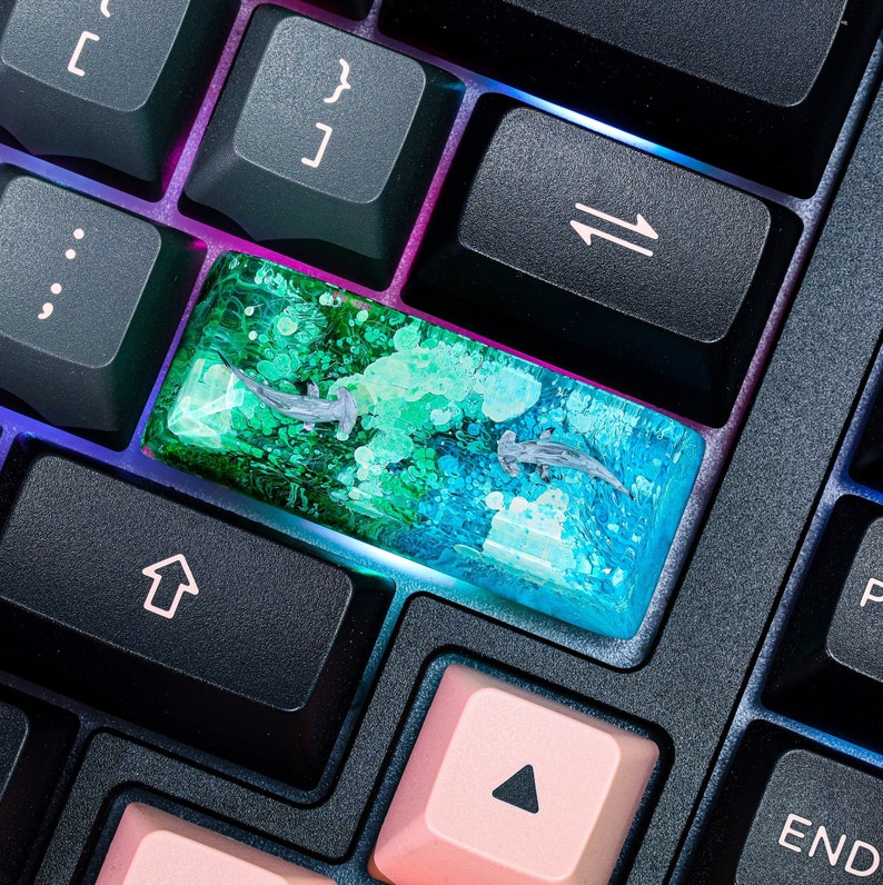 May include: A close-up of a keyboard with a custom keycap. The keycap is made of clear resin with green, blue, and white swirls. The keycap is labeled with the arrow keys.
