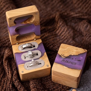 May include: A rectangular wooden ring box with a purple resin inlay, featuring three slots for rings. The lid is engraved with the text Hannah & Sam 10.18.2025. The open box displays three silver-toned rings, including one with a prominent center stone.