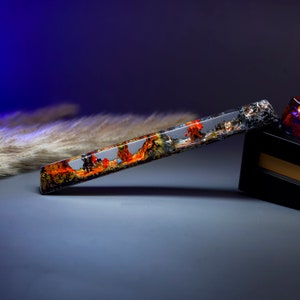 May include: A long, clear resin bar with a black and orange landscape embedded inside. The bar is resting on a black surface.
