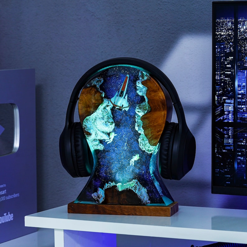 May include: A black headphone stand with a galaxy-themed resin base. The base features a spaceship and a glowing blue and green nebula design.