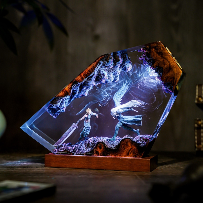 May include: A resin art piece featuring a battle scene with two figures, one wielding a large sword. The artwork is encased in a clear, angled block with a wooden base. The scene is illuminated with blue and white light.