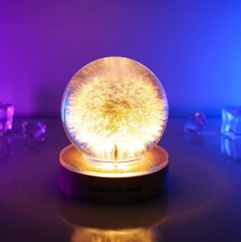 May include: A glass globe with a dandelion inside, illuminated from below, sits on a wooden base with the inscription "To my beautiful wife - I love you".
