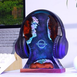 May include: A black headphone stand with a galaxy-themed resin base. The base has a blue, purple, and white galaxy design with a circular logo that says "Starfield".