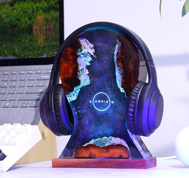 May include: A black headphone stand with a galaxy-themed resin base. The base has a blue, purple, and white galaxy design with a circular logo that says "Starfield".
