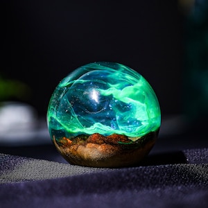 May include: A green and blue resin sphere with a swirling pattern inside. The sphere is sitting on a black surface.