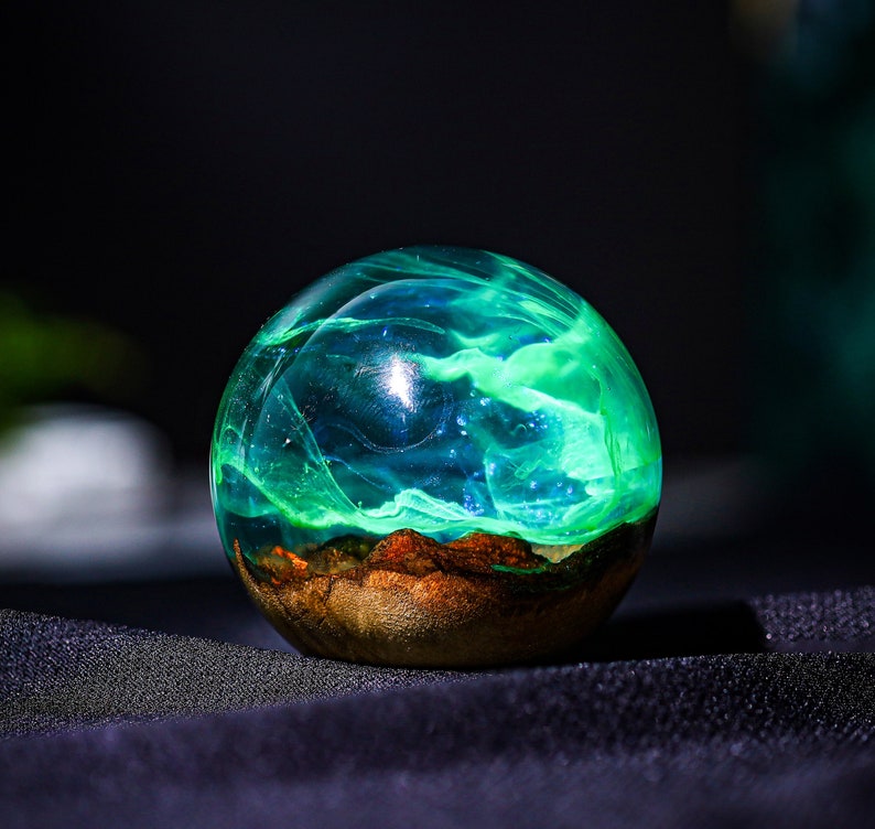 May include: A green and blue resin sphere with a swirling pattern inside. The sphere is sitting on a black surface.