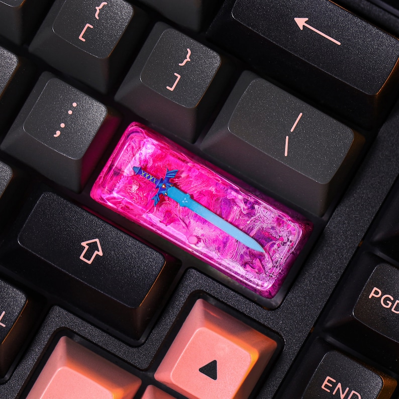 May include: A pink and blue keyboard keycap with a blue sword design. The keycap is made of resin and has a swirling pattern.