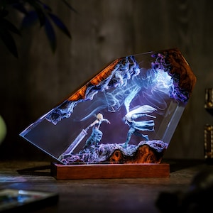 May include: A decorative resin sculpture featuring a battle scene with two figures, set within a clear, angled block. The sculpture has a wooden base and the resin is accented with blue and purple hues, creating a dynamic and artistic display.